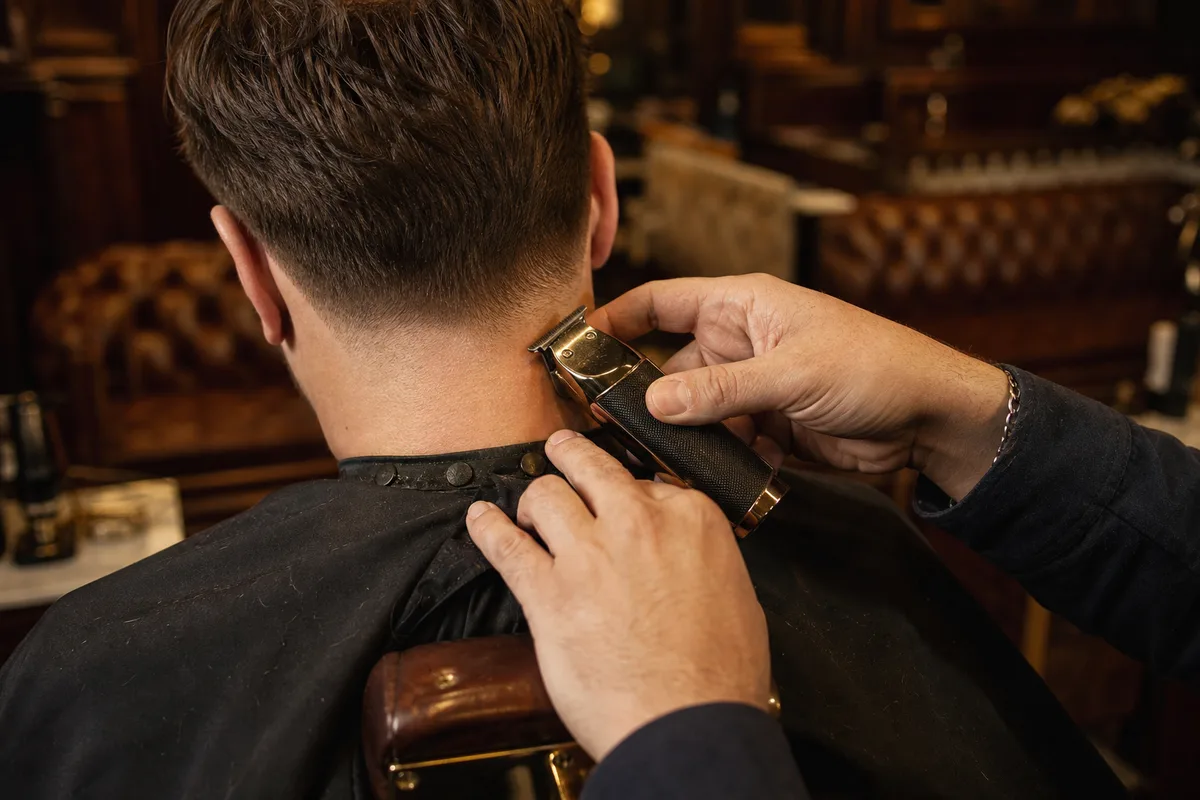 Un coiffeur termine un contour de nuque à la tondeuse sur un client