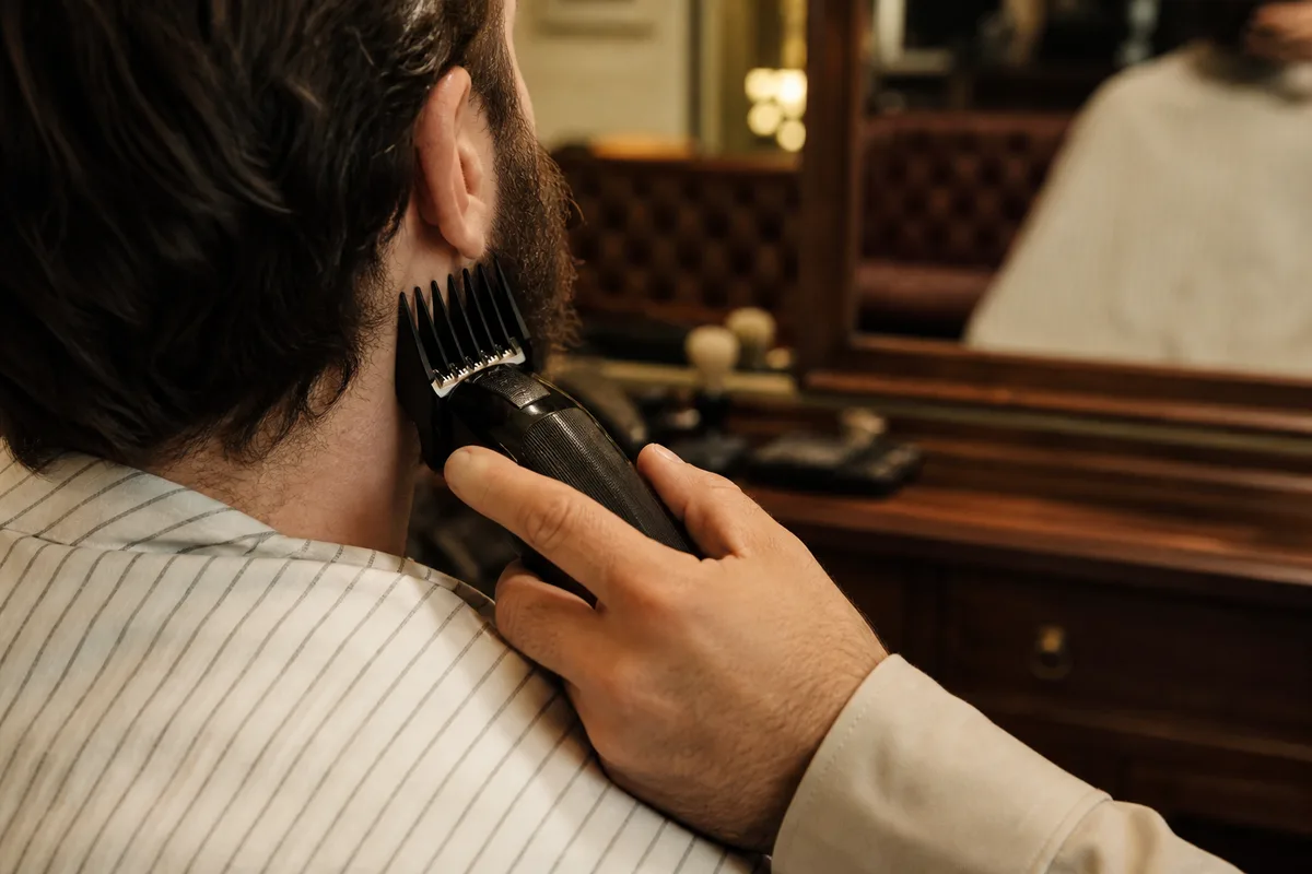Taille d’une barbe à la tondeuse avec sabot devant un miroir
